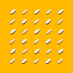 Different pharmaceutical white medicine pills, tablets and capsules on bright yellow background. Medicine creative concepts. Flat lay top view