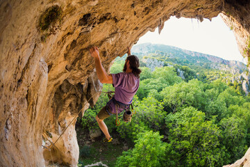 Naklejka premium Rock climber climbs into the cave, Rock in the form of an arch