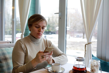 Woman with smartphone and tea in cafe