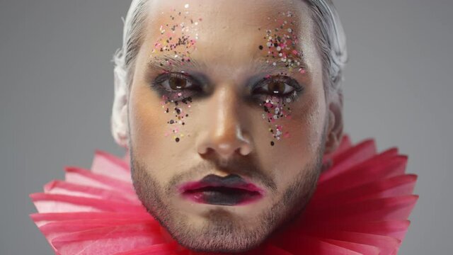 Close up of face of high fashion male model with theatrical make-up with glitter and red ruff around his neck looking at camera