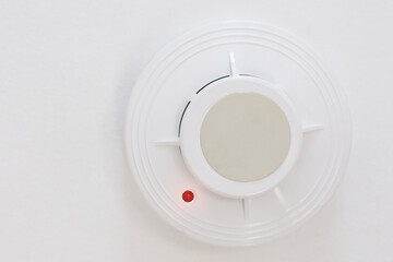 Fototapeta na wymiar A smoke detector hangs on the white ceiling. Fire prevention device in the home or office. Fire safety system. Close-up with space to copy.