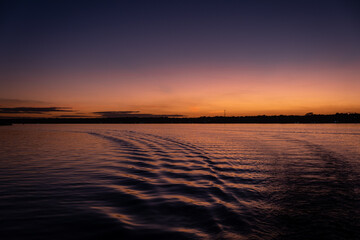 Obraz premium sunset over water from a boat. boat trails. Orange sky