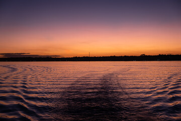 Obraz premium sunset over water from a boat. boat trails. Orange sky
