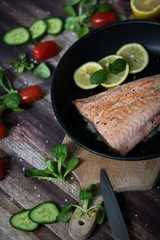 Poster Salmon in a pan with lemon and other vegetables. Salmon on plates © Margo