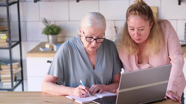Woman teaching senior mother to use internet at home. Senior woman with her daughter looking at modern gadget indoors. close up view. Slow motion nvideo. stock footage