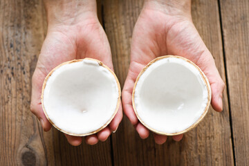 cut half coconut in hand and fresh coconuts on old wooden table for food.