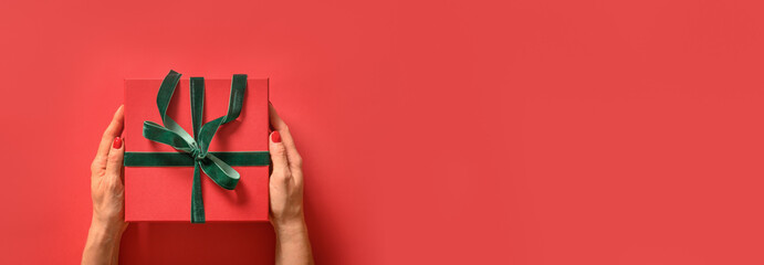 Christmas gift in hand with green ribbon on red background. Banner. Greeting card. Top view. Xmas holiday.