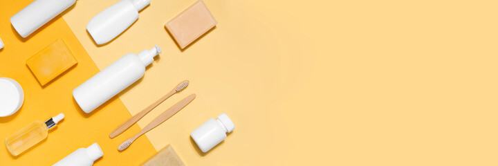 Banner with cosmetic mock up. Tubes with cream, glass bottle with oil, toothbrush, soap, dispensers and jars on yellow background. Flat lay copy space