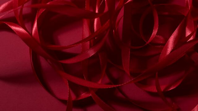 Dark red silk glossy ribbon is falling down on matte deep cherry red surface. Atmospheric video background. New year, Christmas, St. Valentine festive mood 4k still high quality top shot video footage