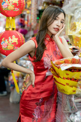 Asian woman wearing red Cheongsam dress shopping at market for Chinese New Year.