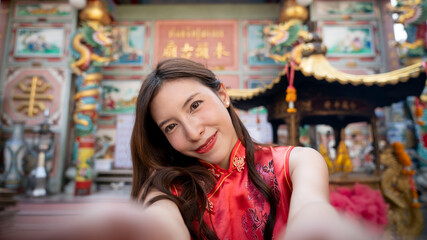 Fototapeta na wymiar Asian woman wearing red Cheongsam dress at Chinese shrine. Chinese new year concept.