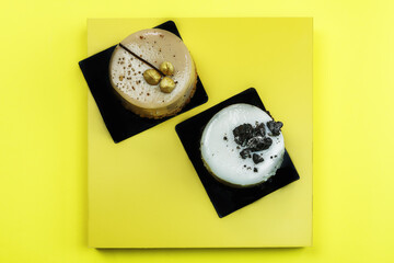 Sweet pastries on display platform top view. Flat lay closeup on a yellow surface, with white and dark chocolate cakes with trim decoration on top.