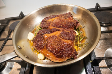 Ribeye beef steak in a stainless steel pan with butter.