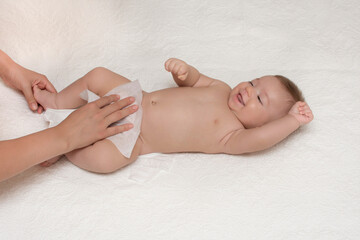 Obraz premium Close up of mother cleaning up baby by wet tissue when changing nappies or diaper in white nursery with bed. Hygiene concept. Cleaning wipe, pure.
