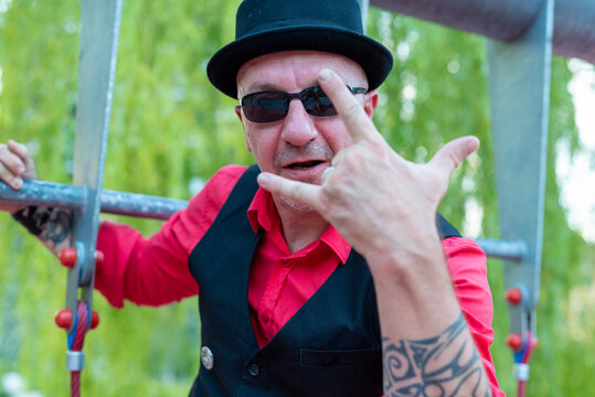 adult man with bowler hat and sunglasses makes a gesture with his hand, symbol of rock music and the ILY concept, portrait of an eccentric and out-of-the-ordinary person