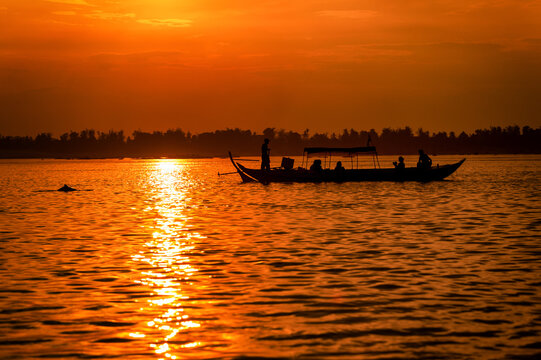 DOLPHIN WATCHING, MEKONG RIVER, KRATIE PROVINCE, CAMBODIA - 31 January 2012: Tourist on boat at sunset hoping to see the elusive irrawaddy dolphin. It's behind them.