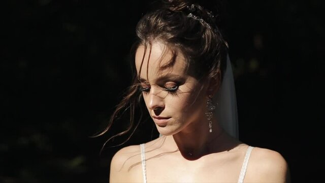 Portrait of a delightful bride in a veil with beautiful makeup and original jewelry in the rays of the sun in nature