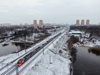 Tracking shot the movement of a high-speed passenger train on a bridge over the river against the backdrop of the city in winter. Travel by rail.