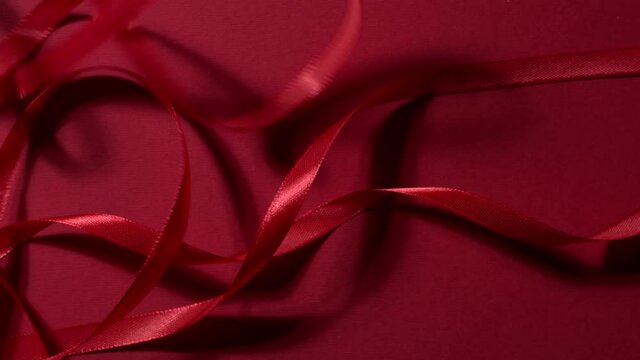 Deep ruby colored silk ribbons are dropping down on a matte cherry red backdrop. Top shot. Atmospheric seamless video background. New year, Christmas festive mood 4k still high quality video footage