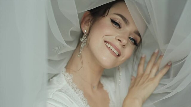Portrait of a stunningly beautiful bride with beautiful makeup and original jewelry in a white veil near the face