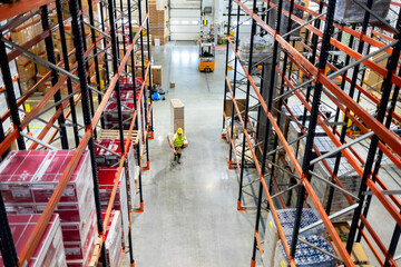 Warehouse worker pulling a pallet truck between shelves, above view