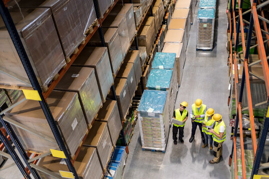 Warehouse workers at work between rows of tall shelves full of packed boxes, top view