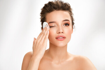 Woman removing makeup, holds cotton pads near face. Photo of woman with perfect skin on white...