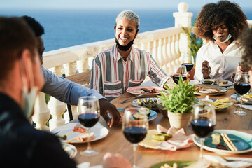 Young multiracial group of friends having dinner and wearing protective masks under chins - Social distance concept - Focus on left girl face
