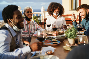 Young multiracial group of friends having dinner and wearing protective masks under chins - Social distance concept- Focus on african girl face