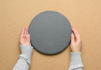 hand hold empty round slate kitchen board on a brown background
