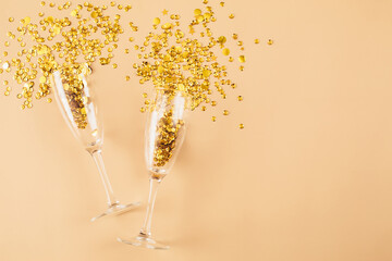 Glasses with gold confetti tinsel on beige background. Flat lay, top view, copy space. Celebrate...