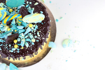 Birthday cake with yellow and blue decor and chocolate icing on a white plate. Cake decorated with lollipops and meringue splinters.