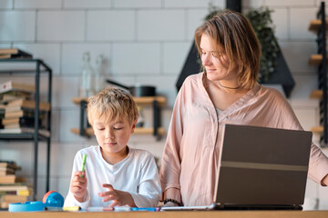 multi tasking, freelance and motherhood concept working at home as her cute little boy plays on a tablet alongside her as she works