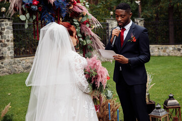 Handsome African American man with beautiful white woman stand near decorated arch, adorable couple...