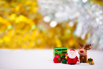 Merry Christmas and Happy New Year concept. Resin or Ceramic Santa Claus and friend standing on white soft floor. Glittering gold and silver background.