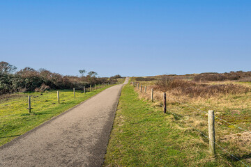 A seemingly endless cycling and walking path through the Dutch dunes on the North Sea near the village of Ouddorp, South Holland province. It's a sunny day in winter and there is no one in the area.