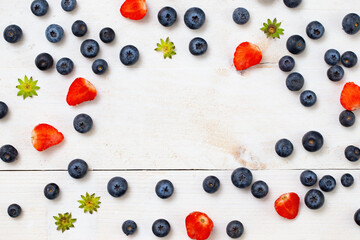 Strawberries cut in half and blueberries arranged on borders of frame with copy space in the middle on white wooden table. Healthy fruit aligned in round shape from directly above.
