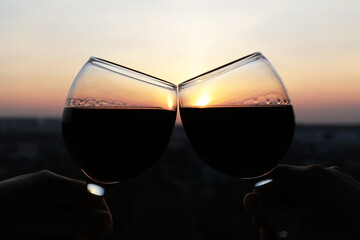 Silhouettes of two glasses with red wine on sunset background, selective focus. Couple clink glasses, concept of celebration, romantic evening at home quarantine, love date