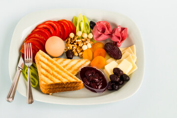 Traditional Turkish Breakfast Plate with salami, cheese, boiled egg, nuts,sliced toast,tomato,jam and olives on light blue surface