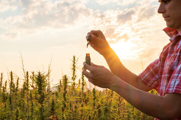 Hemp farmer holding Cbd oil made of Cannabis sativa plant in a dropper and bottle.