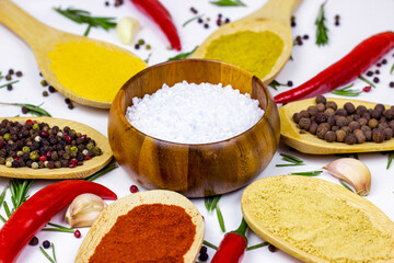 Variety of spices and seasonings (indian curry, different pepper, paprika powder, salt, dry ginger and curcuma) for cooking in wooden spoons on white kitchen table background.