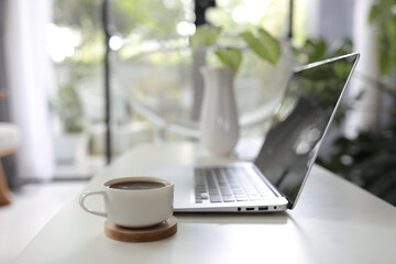 laptop and coffee cup and plant pot on wooden table in front of windows glass door
