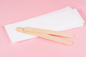 Wax strips for epilation and wooden sticks on pink background