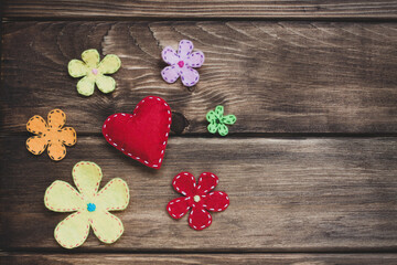 Red felt heart with white stitches and decorative flowers on a vintage wood texture. Love and romantic concept. 
