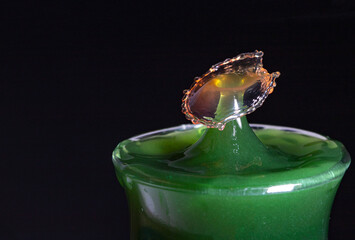Water droplets, green coloured water in the glass, with red droplets falling to collide.