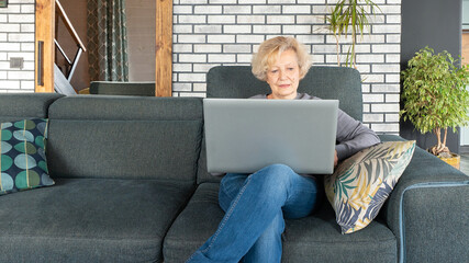 An older adult lady is taking online educational courses and master classes at home on a laptop. The concept of distance online education for older people during covid19 lockdown.