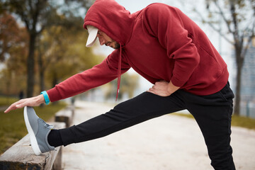 Athletic sporty man training in hoodie sweatshirt in urban city park.