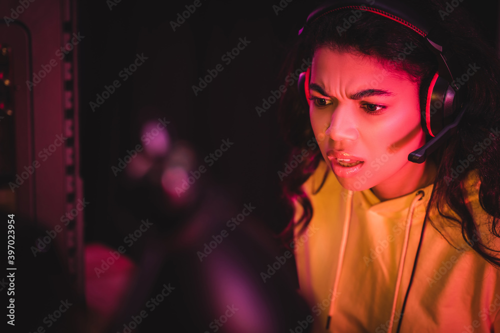 Poster Pensive african american woman in headset looking away near system unit of computer on blurred background