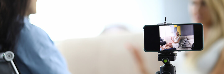 Two women sit and communicate conversation is recorded on smartphone. Journalistic interview from...