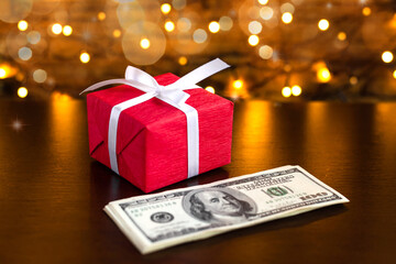 Red gift box on the USA 100 dollar bills on blurred lights background. American dollar. Christmas and New Year money present. Gift cost. Hundred. Finance and business concept. Christmas shopping